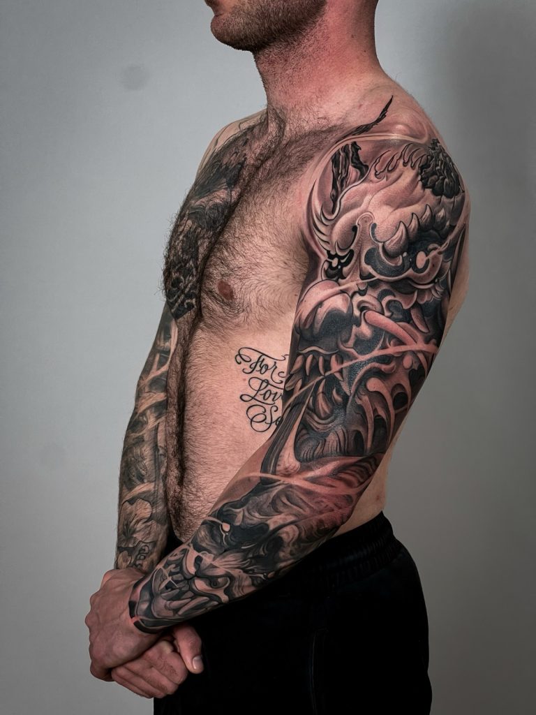 Profile of a full Japanese sleeve where the forearm shows crashing black waves that flow into a horned oni mask and swirling smoke patterns on the upper arm and shoulder.